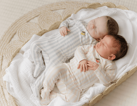 Two babies in matching outfits lying on a textured blanket
